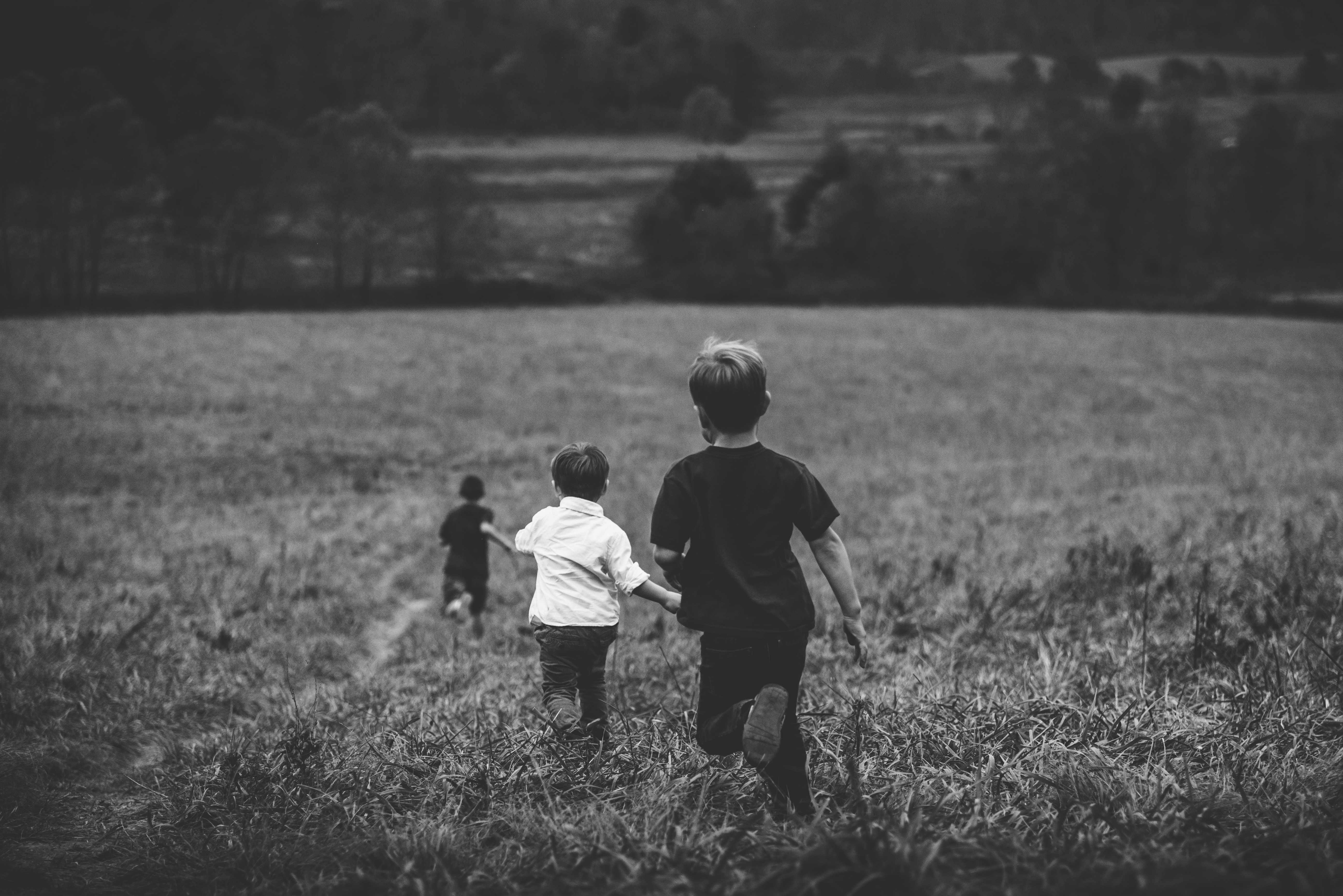 Black and white photo of 3 children running into a field